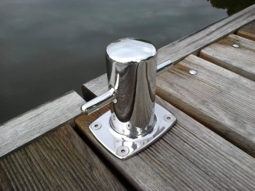 Chromovaný lodní úvazník na dřevěném molu u vody.