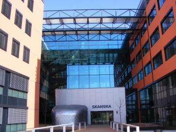 Moderní kancelářská budova Skanska s proskleným atriem a oranžovou fasádou za slunečného dne.