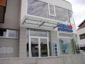 Budova banky Česká spořitelna Dolní Břežany s vitrínou a skleněným přístřeškem nad vstupem.