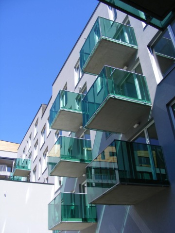 Moderní bytový dům s balkony se skleněným zábradlím.