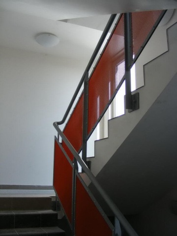 Betonové schodiště s červeným zábradlím a kovovým madlem v moderní budově Milíčovský háj.