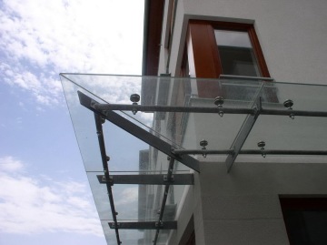 Skleněná přístřešek s kovovou konstrukcí připevněnou na budovu Dolní Břežany, modré nebe v pozadí.