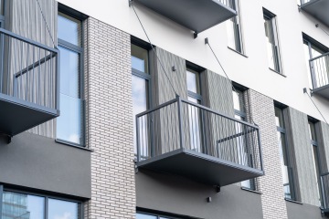 Moderní bytový dům s balkony, skleněnými okny a cihlami.