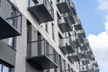 Moderní bytový dům s několika balkony a světlou fasádou pod modrou oblohou.