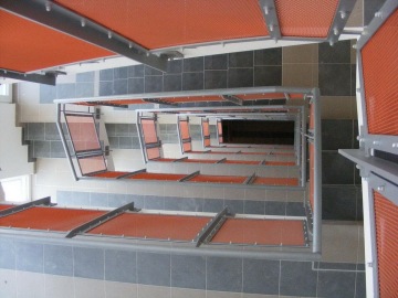 Schodiště s červenými mřížemi a šedými dlaždicemi pohledem shora dolů na sídlišti Milíčovský háj.