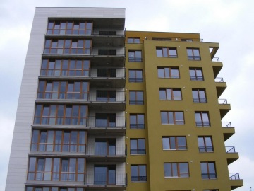 Moderní bytový dům Vokovice s velkými okny a balkony, šedá a žlutá fasáda.