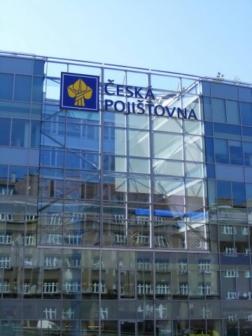 Moderní prosklená budova s logem České pojišťovny a odrazem okolních domů ve skle.