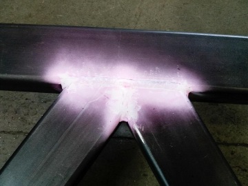 Svařená kovová konstrukce v tmavé dílně, detekce chyb v místě spoje s fluorescenční kapalinou.