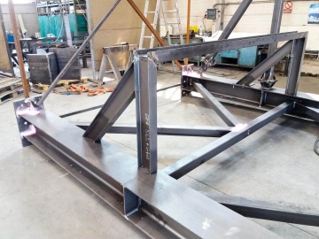 Ocelová konstrukce pod sila ve výrobní dílně s viditelnými nosníky a podpěrami.