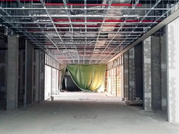 Stavební místo s odkrytým stropem a zelenou plachtou na konci chodby.