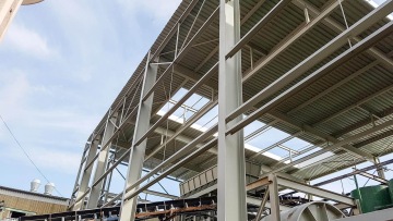 Pohled na ocelovou konstrukci budovy OK haly s otevírací střechou pod modrou oblohou.