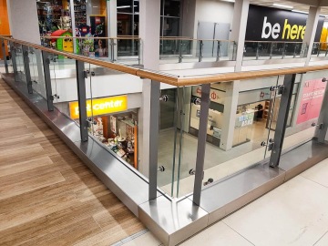 Obchodní centrum s proskleným zábradlím, obchody a barevnými reklamními panely.