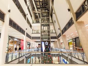 Obchodní centrum s vánočním stromečkem, osvětlené zábradlí a obchody po stranách.