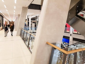 Nákupní centrum s vánočními světly, dvě osoby kráčející po světlé chodbě.