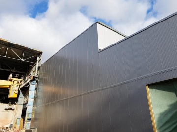 Průmyslová budova OK haly s šedou kovovou fasádou a otevřenou konstrukcí pod modrou oblohou.