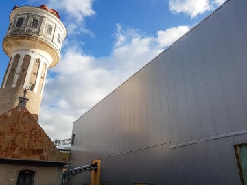 Starý vodojem vedle moderní budovy OK haly pod modrou oblohou s několika oblaky.