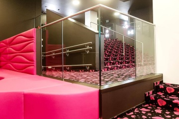 Moderní interiér s růžovou lavicí, skleněným zábradlím a černými schody s růžovým vzorem.