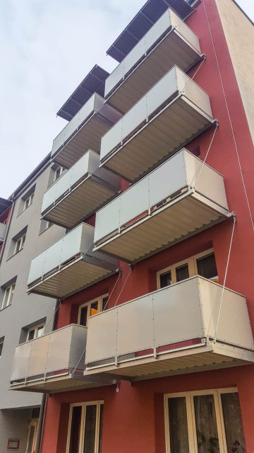 Šedé a červené průčelí budovy s balkony Bechyně ve vertikální linii.