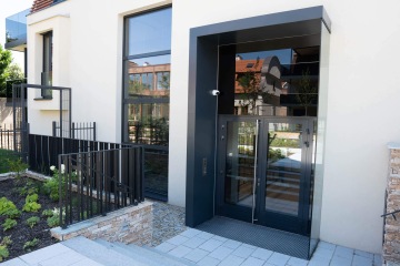 Venkovní výtah u moderní budovy Chateau Troja Residence s prosklenými dveřmi a zábradlím.