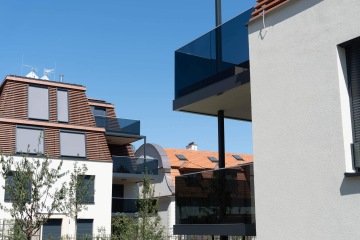 Moderní budovy Chateau Troja Residence s prosklenými balkony a žaluziemi na modré obloze.