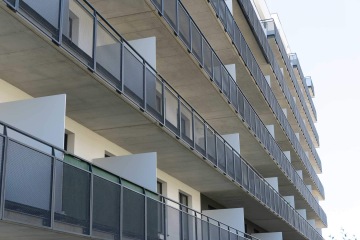 Moderní budova s řadou balkonů se zábradlím s tahokovovou výplní.