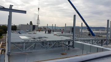 Stavební dělníci na střešní konstrukci Škoda Auto - Centrální kuchyně s jeřábem zvedajícím kovový díl.