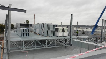 Dělník stojící na střešní konstrukci Škoda Auto - Centrální kuchyně s ventilací, okolní tovární budovy a jeřáb v pozadí.