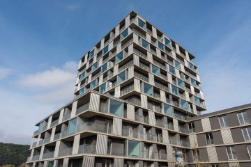 Moderní bytový dům ve Čtvrti Zahálka s balkony a prosklenými stěnami pod modrou oblohou.