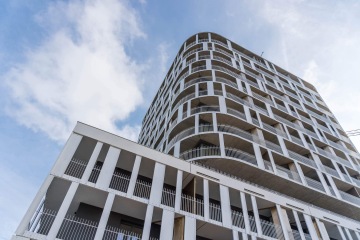 Moderní vícepatrová budova ve Čtvrti Zahálka s bílými balkony proti modré obloze.