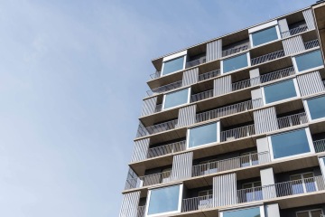 Moderní bytový dům ve Čtvrti Zahálka se skleněnými balkony za slunečného dne.