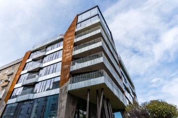 Moderní budova Dům Komunardů XXXV s balkony a kovovým obložením, modrá obloha.