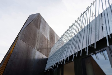 Moderní architektura s kovovými pruty na fasádě Dům Komunardů XXXV a šikmou stěnou pod oblačnou oblohou.