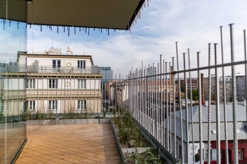 Moderní terasa na Dům Komunardů XXXV s výhledem na městskou krajinu, kovové zábradlí a truhlíky s rostlinami.