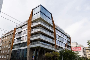 Moderní budova Dům Komunardů XXXV s prosklenými balkony a rezavými kovovými detaily ve městě.