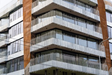 Moderní bytová budova Dům Komunardů XXXV s prosklenými balkony a vertikálními kovovými prvky na fasádě.