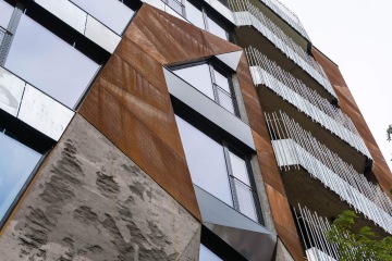 Moderní fasáda budovy Dům Komunardů XXXV s kovovými a skleněnými prvky, texturovanými panely a vertikálními žaluziemi.