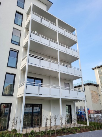 Moderní bytový dům Haardtring Darmstadt s několika patry balkonů, vedlejší cihlová budova, modrá obloha.