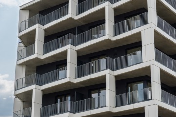Moderní bytová budova s balkony a stříbrnými zábradlími.