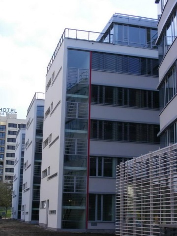 Moderní kancelářská budova Trianon se skleněnými fasádami a červeným pruhem na schodišti.