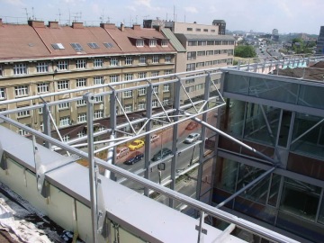 Pohled na střechu budovy České Pojišťovny s ocelovou konstrukcí, městská ulice s projíždějícími auty v pozadí.