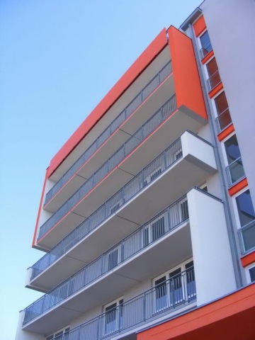 Moderní bytová budova Milíčovský háj s oranžovými balkony a čistou fasádou proti modré obloze.