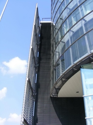 Moderní skleněná budova Trianon s kovovými žaluziemi za slunečného dne.