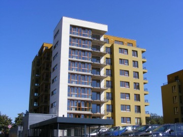 Moderní bytový dům Vokovice s balkony na slunečném pozadí v modré obloze.