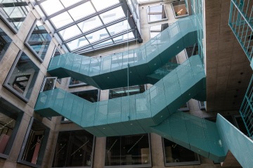 Moderní tyrkysové schodiště v prosklené budově se světlíkem nahoře.