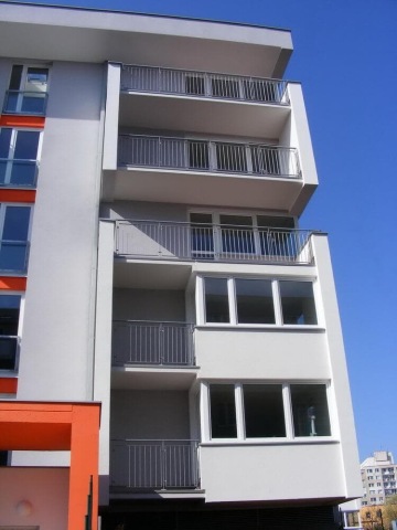 Moderní vícepatrová budova Milíčovský háj s balkony a bílou fasádou na pozadí modré oblohy.