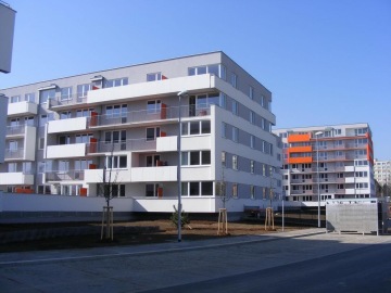 Moderní bytová budova Milíčovský háj s velkými balkóny a oranžovými akcenty na fasádě za slunečného dne.