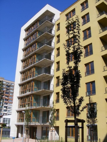 Moderní bytový dům Vokovice s balkony, stromky vysazené před budovou, modrá obloha.