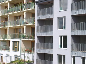 Moderní bytový dům s balkony se skleněným a kovovým zábradlím.