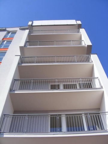 Moderní budova Milíčovský háj s balkóny a kovovými zábradlími proti modré obloze.