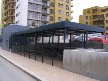 Oplocené parkoviště před moderními bytovými domy Vokovice se zaparkovanými auty.